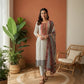 Woman in traditional outfit standing in a room with plants and a chair.
